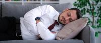 man in white shirt and black tie napping on a couch